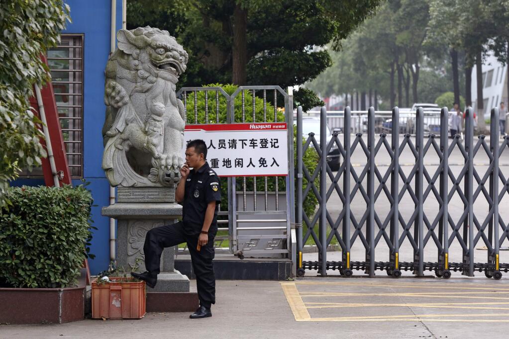 In this June 18, 2017, photo, a security guard smokes near a main entrance gate of the Ganzhou Huajian International Shoe City Co.'s factory, which has made shoes for the Ivanka Trump brand, in Ganzhou in southern China's Jiangxi Province. The sign reads 'visitors please exit the vehicle and register, people without relevant reasons cannot enter this important factory area.' (AP Photo/Andy Wong)