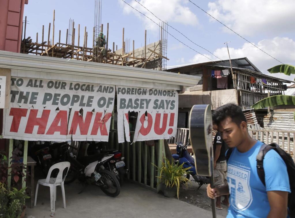 A resident walks past a sign thanking foreign and local donors in the rehabilitation of typhoon-ravaged Basey township, Eastern Samar province in central Philippines, Thursday, Nov. 6, 2014. Some survivors are still housed in tents almost a year after Typhoon Haiyan ravaged Leyte, Eastern Samar and other provinces in central Philippines that killed thousands and left a wide swath of destruction. On Saturday, Nov. 8, the country will mark the first year anniversary of the super typhoon. (AP Photo/Bullit Marquez)