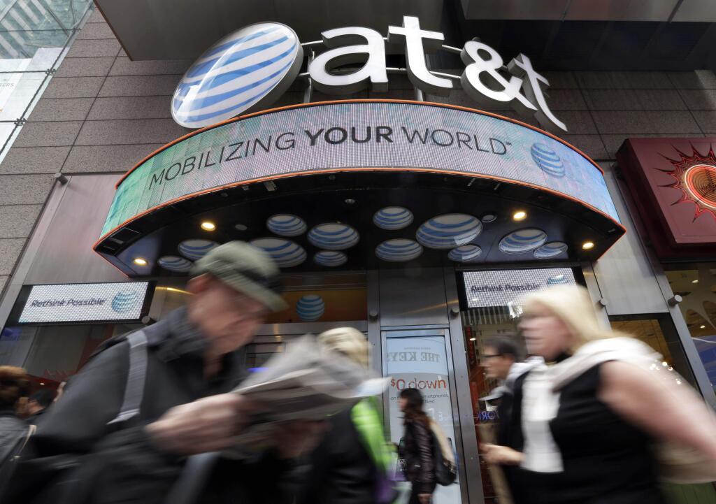 In this Oct. 21, 2014 photo, people pass an AT&T store in New York's Times Square. AT&T is being sued by the government over allegations it misled millions of smartphone customers who were promised unlimited data but had their Internet speeds cut by the company ó slowing their ability to open web pages or watch streaming video. (AP Photo/Richard Drew)