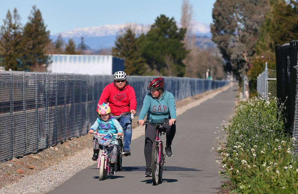 Evelia, right, Luis Castaneda, and their daughter Lily, 5, ride their bikes along the existing shared use path along the SMART tracks, north of Bellevue Avenue, in Santa Rosa on Monday, February 18, 2019. An extension of the shared use path south of Bellevue Avenue is part of a new master plan for bike routes and walking paths before the planning commision.(Christopher Chung/ The Press Democrat)