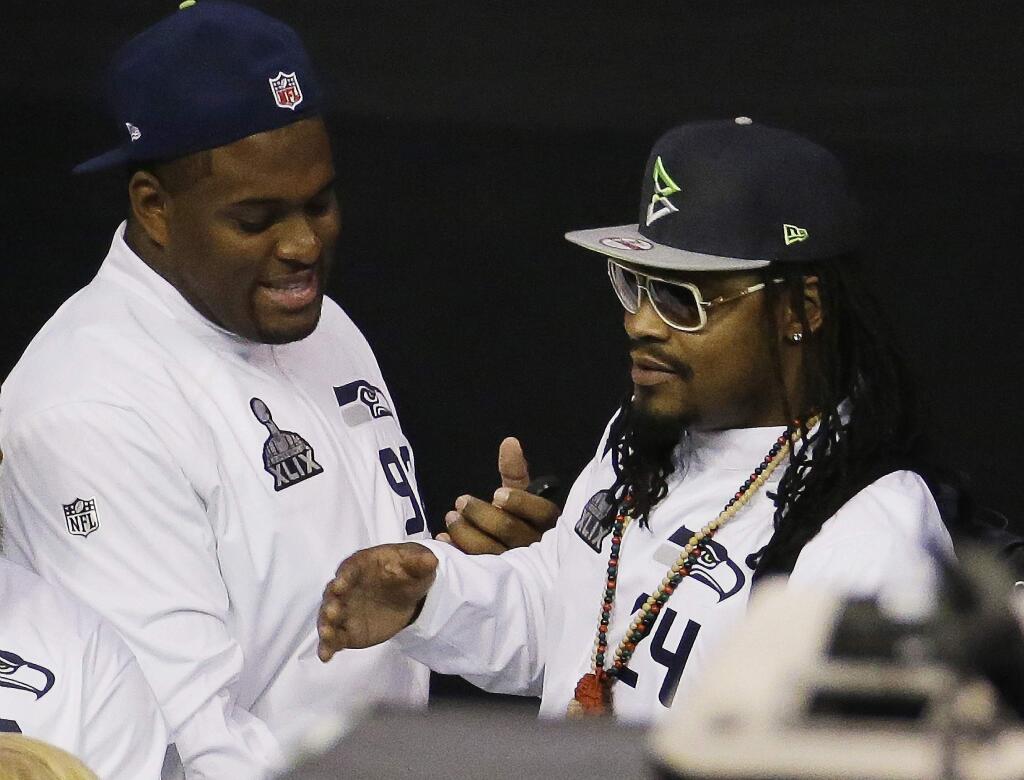 Seattle Seahawks' Marshawn Lynch, right, talks to teammate Brandon Mebane as he makes his way out off the floor at the beginning of media day for NFL Super Bowl XLIX football game Tuesday, Jan. 27, 2015, in Phoenix. (AP Photo/Charlie Riedel)