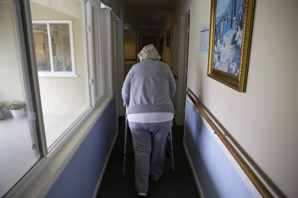 FILE - In this Dec. 5, 2019, file photo, a woman walks to her room at a senior care home in Calistoga, Calif. California Gov. Gavin Newsom's plan to cover a $54.3 billion budget deficit includes slashing spending that keeps more than 45,000 people out of nursing homes, one of a series of cuts targeting older adults who are among the most at risk for the new coronavirus. The cuts have angered state lawmakers from both political parties who say it's irresponsible in light of the coronavirus pandemic that has spread through nursing homes across the state. (AP Photo/Eric Risberg, File)