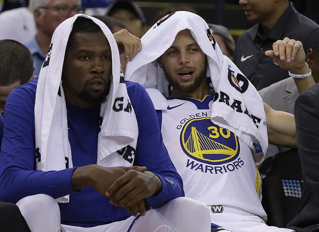 Golden State Warriors' Kevin Durant, left, and Stephen Curry watch from the bench during the first half of a pre-season NBA basketball game against the Denver Nuggets Saturday, Sept. 30, 2017, in Oakland, Calif. (AP Photo/Ben Margot)