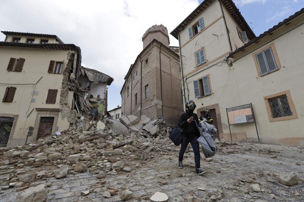 A resident carrying his belongings passes in front of the collapsed bell tower of the Santa Maria in Via church in the town of Camerino, in central Italy, Thursday, Oct 27, 2016, after a 5.9 earthquake destroyed part of the town. Authorities began early Thursday to assess the damage caused by a pair of strong quakes in the same region of central Italy hit by the deadly August temblor, as local officials appealed for temporary housing adequate for the cold mountain temperatures with winter's approach. (AP Photo/Alessandra Tarantino)