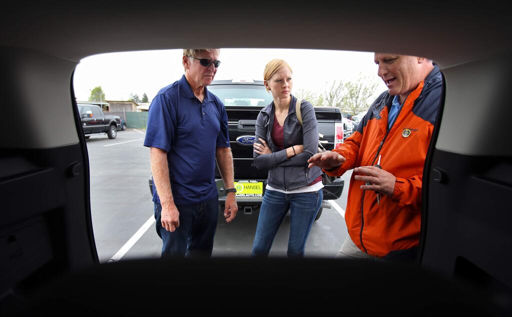 Hansel Ford sales and leasing consultant Jeremy Aust, right, shows features of the cargo area in a new Ford Escape to Lindsey Hazlewood and her father, John, at the dealership in Santa Rosa on Friday, March 27, 2015. (Christopher Chung/ The Press Democrat)
