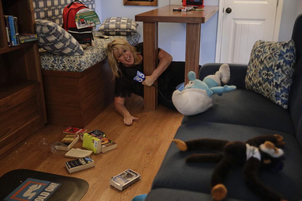 TV reporter Wendy Burch takes cover under a table in a Big Shaker simulating a 6.8 magnitude earthquake Thursday, Oct. 18, 2018, in Los Angeles. Millions of people around the world are practicing the basic earthquake safety skill of 'drop, cover and hold on.' Thursday marks the 10th anniversary of the 'Great ShakeOut' earthquake drills that originated in Southern California. (AP Photo/Jae C. Hong)
