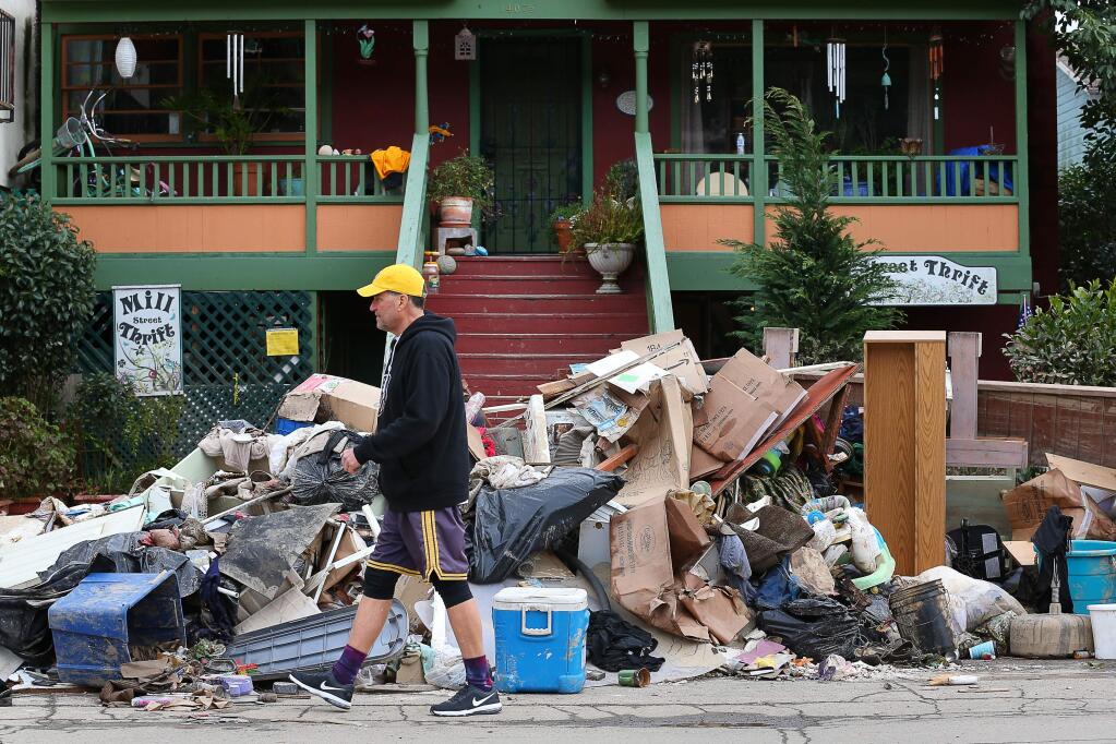 Jack Seely walks past a pile of flood damaged materials along Mill Street in Guerneville on Monday, March 4, 2019. (CHRISTOPHER CHUNG/ PD)