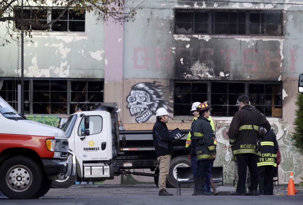 FILE - In this Monday, Dec. 5, 2016, file photo, emergency crews work in front of the site of a massive warehouse fire in Oakland, Calif. Micah Allison, the wife of the founder of a ramshackle Oakland artists' colony where dozens of people burned to death in a fire last month says she's sorry about what happened but is angry about what she called 'pretty terrible' treatment by the media and ex-neighbors. (AP Photo/Marcio Jose Sanchez, File)