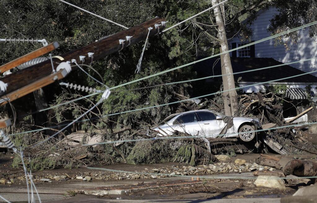FILE - In this Jan. 10, 2018, file photo, a damaged car sits over fallen and debris behind downed power lines in Montecito, Calif. While an aggressive cleanup could mean Montecito will welcome visitors again in weeks, the rebuilding of infrastructure and hundreds of homes will be measured in months and years. It will also offer a chance to re-imagine aspects of a town that has favored slow growth over the runaway development closer to Los Angeles, 90 miles down the coast. (AP Photo/Marcio Jose Sanchez, File)