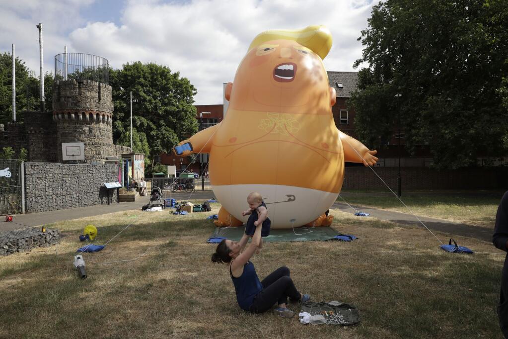 In this photo taken on Tuesday, July 10, 2018, Ruth Armitage and her nine-month old baby Ivy pose for the media in front of a six-meter high cartoon baby blimp of U.S. President Donald Trump during a practice session in Bingfield Park, north London. Trump will get the red carpet treatment on his brief visit to England that begins Thursday: Military bands at a gala dinner, lunch with the prime minister at her country place, then tea with the queen at Windsor Castle before flying off to one of his golf clubs in Scotland. But trip planners may go out of their way to shield Trump from viewing another aspect of the greeting: an oversize balloon depicting the president as an angry baby in a diaper that will be flown from Parliament Square during what are expected to be massive gatherings of protesters opposed to Trump's presence. (AP Photo/Matt Dunham)