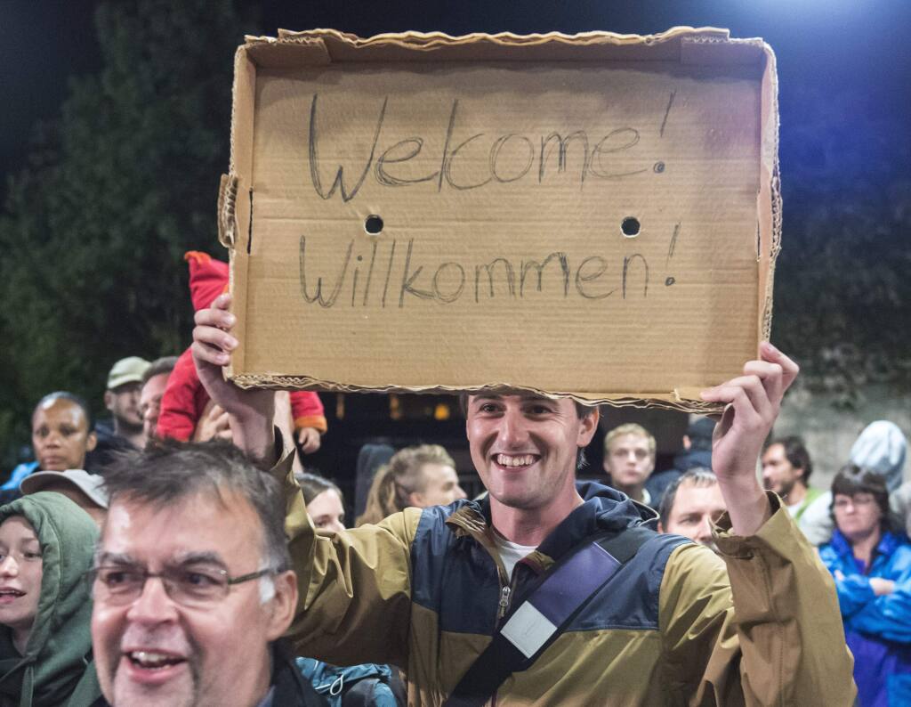 Am man holds a cardboard with a 'Welcome' slogan during the arrival of refugees at the train station in Saalfeld, central Germany, Saturday, Sept. 5, 2015. Hundreds of refugees arrived in a train from Munich to be transported by busses to an accomodation centre. (AP Photo/Jens Meyer)