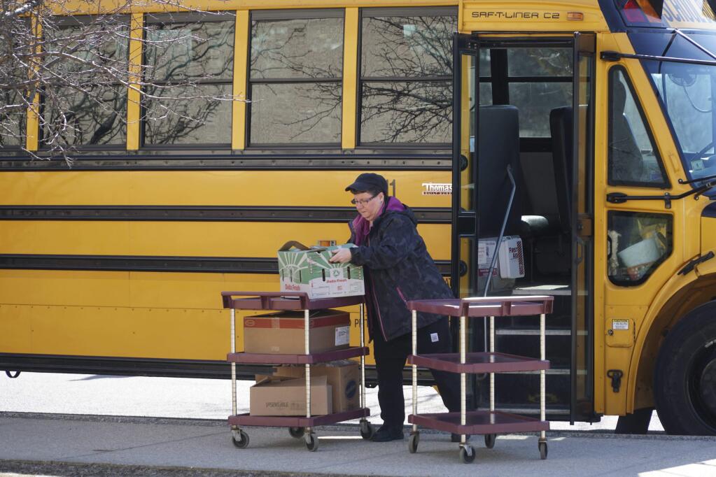 Cafeteria workers fill buses to distribute grab and go lunches from Conte Community School in Pittsfield, Massachusetts, Monday, March 16,2020. The lunches provide a good meal for children while schools are closed due to coronavirus. (Ben Garver/The Berkshire Eagle via AP)