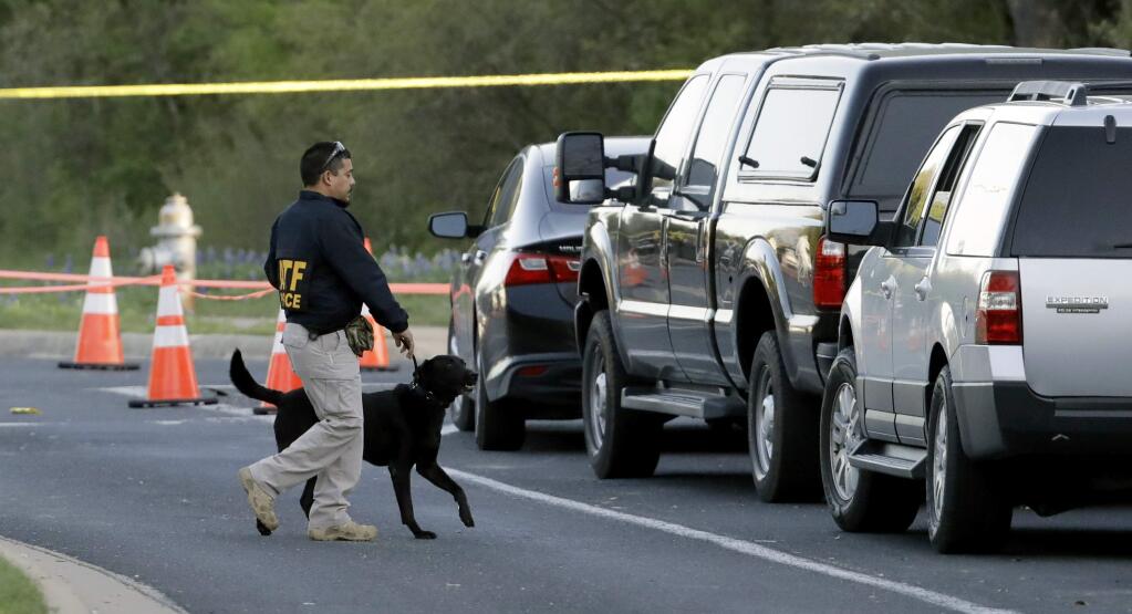 An agent the Bureau of Alcohol, Tobacco, Firearms and Explosives works with his dog near the site of Sunday's explosion, Monday, March 19, 2018, in Austin, Texas. Fear escalated across Austin on Monday after the fourth bombing this month - this time, a blast that was triggered by a tripwire and demonstrated what police said was a 'higher level of sophistication' than the package bombs used in the previous attacks. (AP Photo/Eric Gay)