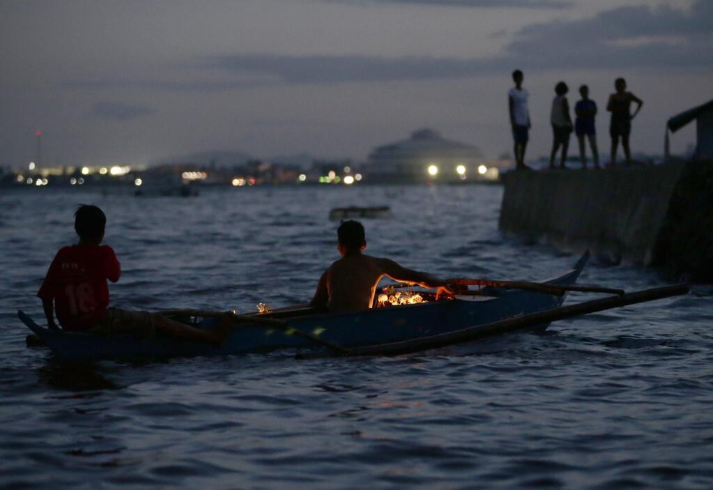 Typhoon survivors paddle out to sea to float flowers at a coastal village in Tacloban city, Leyte province in central Philippines Saturday, Nov. 8, 2014 to commemorate the moment when Haiyan barreled inland from the Pacific with ferocious winds and tsunami-like waves, leaving more than 7,300 dead or missing and leveling entire villages in the world's deadliest disaster last year. (AP Photo/Bullit Marquez)
