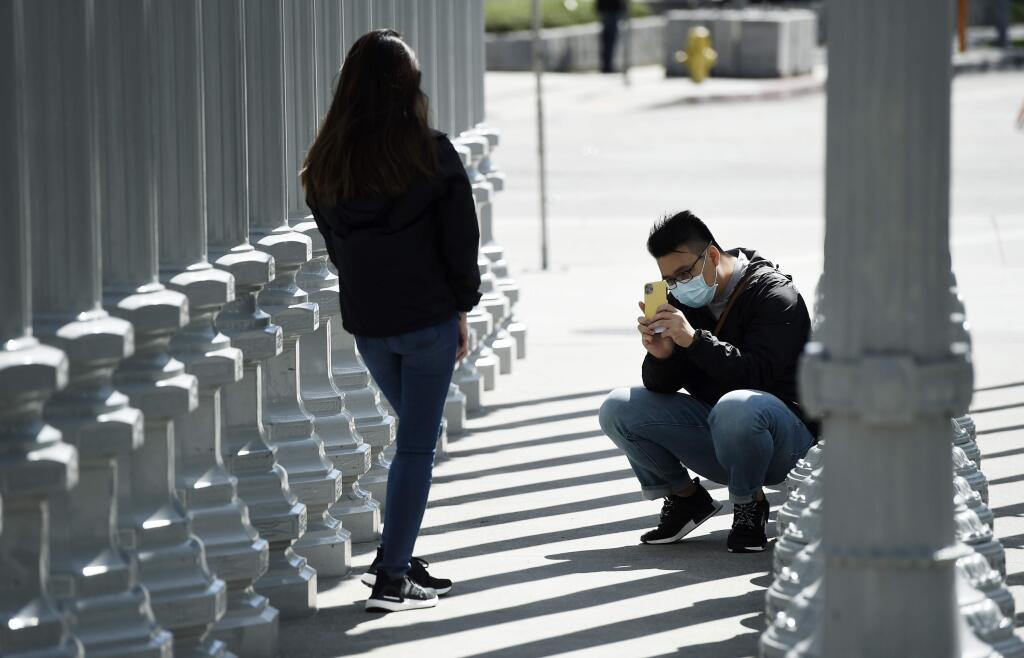 Visitors to artist Chris Burden's 'Urban Light' art installation outside the Los Angeles County Museum of Art take pictures of each other, Wednesday, March 18, 2020, in Los Angeles. (AP Photo/Chris Pizzello)