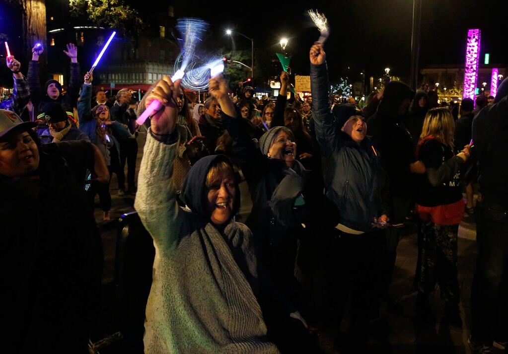 Mary Anne Hunt-Valencia, front, Ina Welker, and Brenda Haas, right, and wave their lighted wands in the air with other attendees during a vigil to bring the community together in the wake of the fires around Sonoma County, at Old Courthouse Square in Santa Rosa, California on Friday, October 20, 2017. (Alvin Jornada / The Press Democrat)
