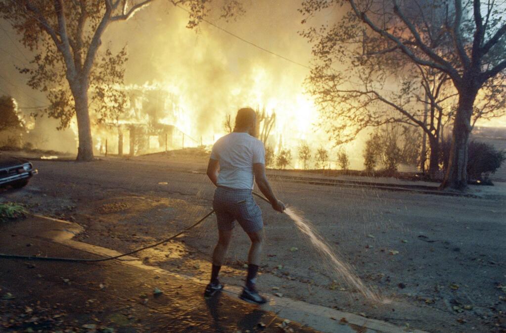 Berkeley resident Jim Beatty stands hopelessly with a garden hose as homes burn out of control in the Berkeley and Oakland hills area on Sunday, Oct. 20, 1991 in Berkeley, California. A wind-driven fire roared through an upscale residential area in the hills above Oakland on Sunday, engulfing hundreds of homes and killing five people, authorities said. (AP Photo/Kevin Rice)
