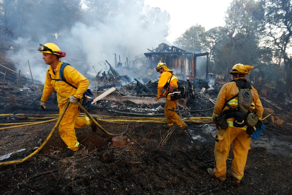 Lake County firefighters Cory Smith, left, Alex Thoman and engineer/paramedic Adam Thoman pull hose to mop up after a wildfire burned through a residential area off Lake Street in Lower Lake, California on Tuesday, August 9, 2016. (Alvin Jornada / The Press Democrat)