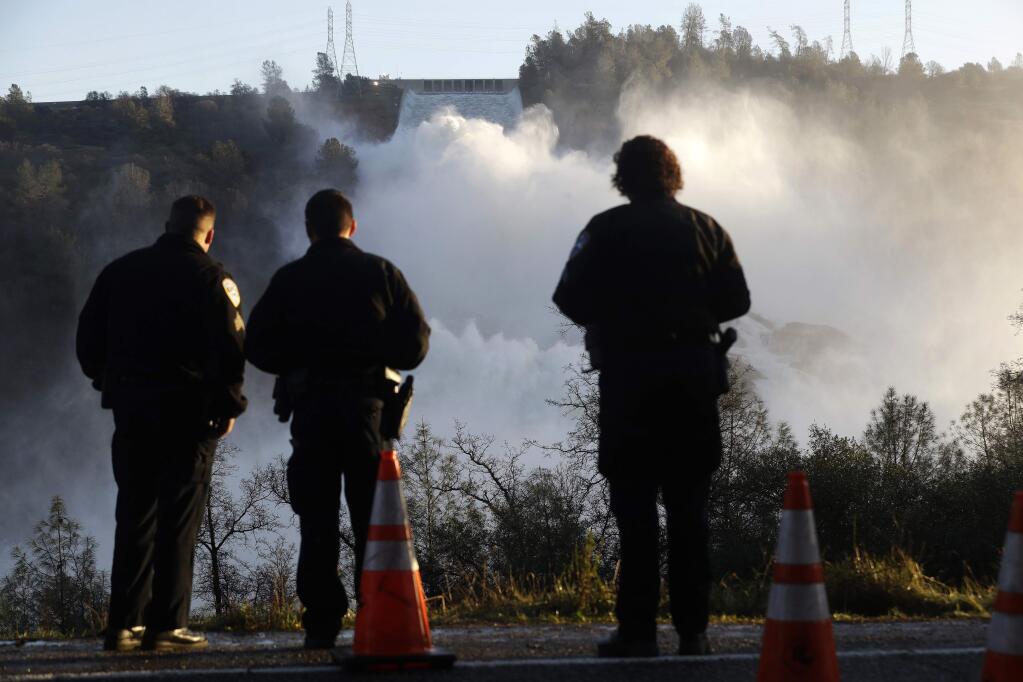 FILE- In this Feb. 14, 2017, file photo, police officers watch the Oroville Dam's main spillway from a lookout point in Oroville, Calif. A team of experts is warning of a 'very significant risk' if the main spillway of the California dam is not operational again by the next rainy season. The warning is contained in a report obtained Wednesday, March 22 by The Associated Press. (AP Photo/Marcio Jose Sanchez, File)