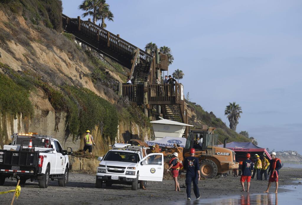 FILE - In this Friday, Aug. 2, 2019 lifeguards and search and rescue personnel work at the site of a cliff collapse at a popular beach in Encinitas, Calif. Three family members enjoying a day at a San Diego area beach were killed Friday when a huge slab of the cliff above plunged on to the sand. The collapse has raised questions about the stability of bluffs along California's 1,000-mile (1,600-kilometer) coast. (AP Photo/Denis Poroy, File)