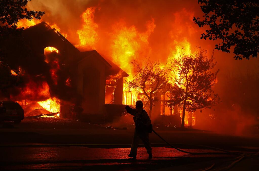 A firefighter walks past homes that are fully engulfed in flames near Altruria Drive in the Fountaingrove area of Santa Rosa on Monday, October 9, 2017. (Christopher Chung/ The Press Democrat)