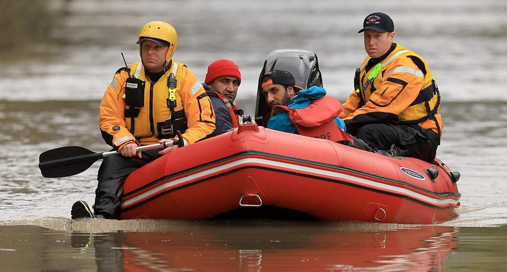 Mark Haas, left, and Jason Clopton of the Russian River Fire District swift water rescue team, motor to shore after rescuing Vikram and Sunny Singh who were flooded out of the second story of MD Gas and Liquor. Store on River Road in Guerneville. (Kent Porter / The Press Democrat) 2019