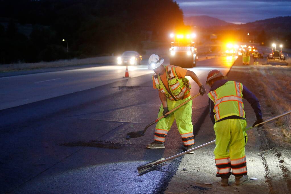 Christopher Mann, left, and Luis Perez of DeSilva Gates Construction follow behind a paving machine and fill holes in the base layers of asphalt their crew is applying on the number one lane of southbound Highway 101 near Geyserville, California, on Wednesday, May 16, 2018. (Alvin Jornada / The Press Democrat)
