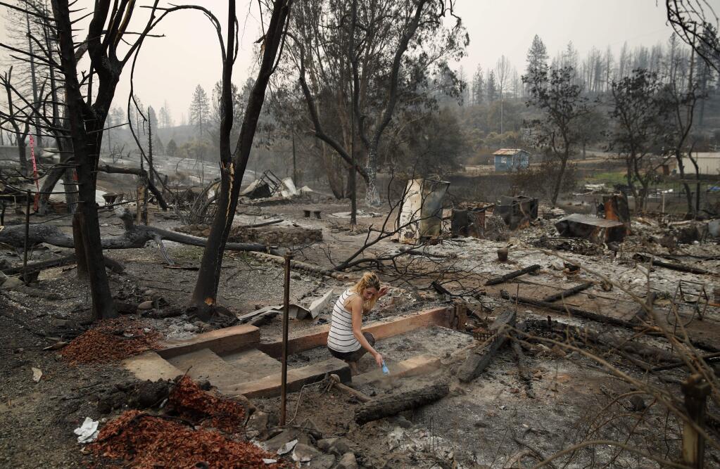 Bree Seville uses a small brush to sweep the stairs leading to burned out ruins of her fiancee's mother's home in the Keswick area of Redding, Calif., Thursday, Aug. 9, 2018. California is seeing earlier, longer and more destructive wildfire seasons because of drought, warmer weather attributed to climate change and home construction deeper into the forests. (AP Photo/John Locher)