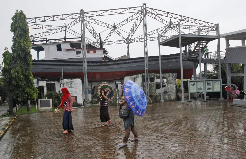Acehnese women walk past a damaged house on which a fishing boat landed after it was swept away by the Indian Ocean tsunami 10 years ago, in Banda Aceh, Aceh province, Indonesia, Thursday, Dec. 25, 2014. Aceh, the worst-hit region by the 2004 tsunami, is preparing to commemorate the 10th anniversary of the Boxing Day tsunami that killed more than 100,000 people in the province. The boat and the house are now preserved as a monument. (AP Photo/Binsar Bakkara)