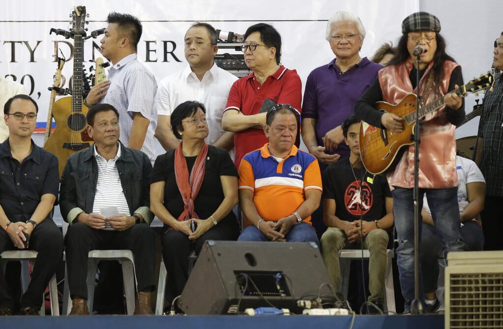 Philippine President Rodrigo Duterte, second from left, looks as Filipino folk singer Freddie Aguilar sings during the solidarity dinner with the poor event at a slum area in Manila, Philippines on Thursday, June 30, 2016. Duterte was sworn in Thursday as president of the Philippines, with many hoping his maverick style will energize the country but others fearing he could undercut one of Asia's liveliest democracies amid his threats to kill criminals en masse. (AP Photo/Aaron Favila)
