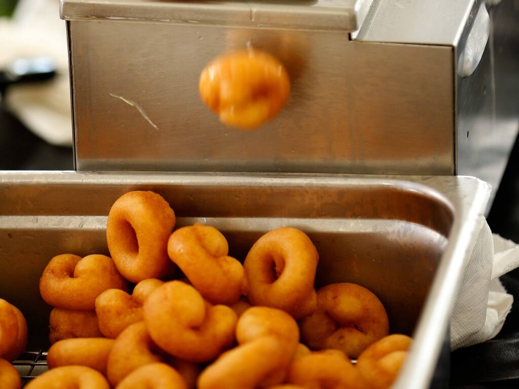Mini doughnuts tumble into a tray from a semi-automated doughnut-making machine from Harvey's Gourmet Donuts. (Alvin Jornada / The Press Democrat)