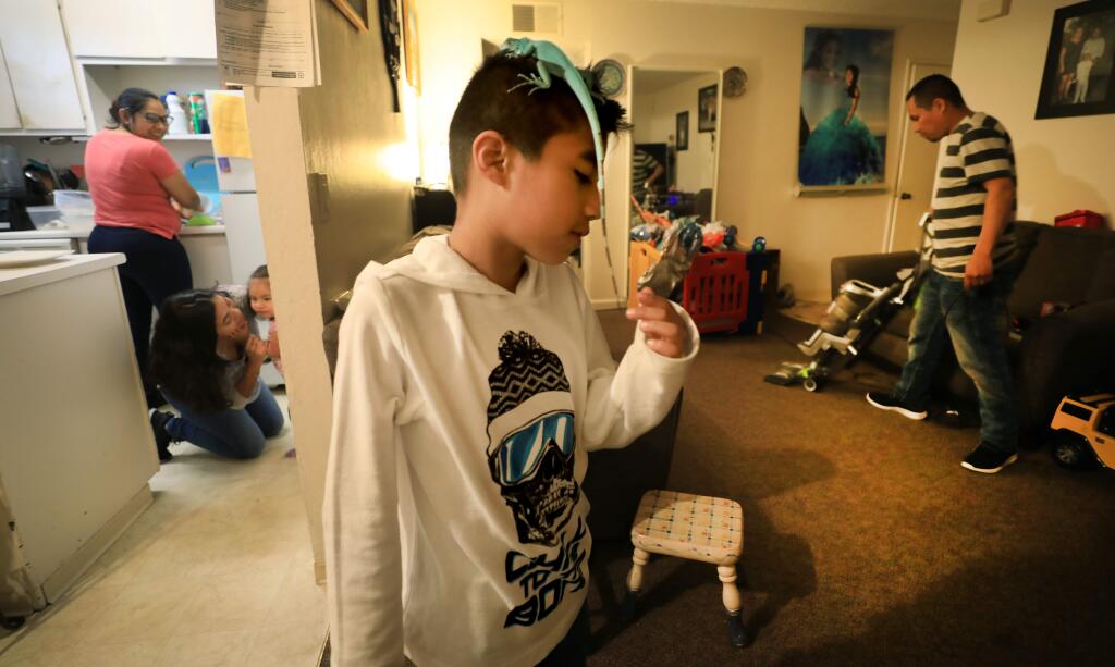 Oliver Ramirez, 8, pets the tail of Frozone, the family's pet iguana, as his mom Edith Vargas, left, and dad, Jorge Ramirez, clean house. Sister Nancy Ramirez, 19, plays with youngest sibling, 2-year-old Daleyza Ramirez, Wednesday, April 3, 2019 in Healdsburg. The apartment complex where they live is being purchased by Burbank Housing for $5 million, to keep the complex affordable to its residents. (Kent Porter / Press Democrat) 2019