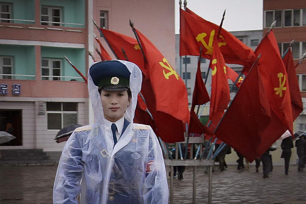 A North Korean traffic police woman directs vehicles at a street junction while behind her the sidewalk is decorated with flags of the ruling party, the Workers' Party (WON MAY-E / Associated Press)