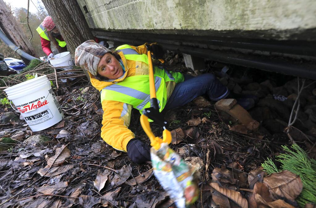 Volunteer Debbie Grima-Lowe climbs under the Guerneville foot bridge to collect trash left after the flooding of the Russian River last week. (John Burgess/The Press Democrat)