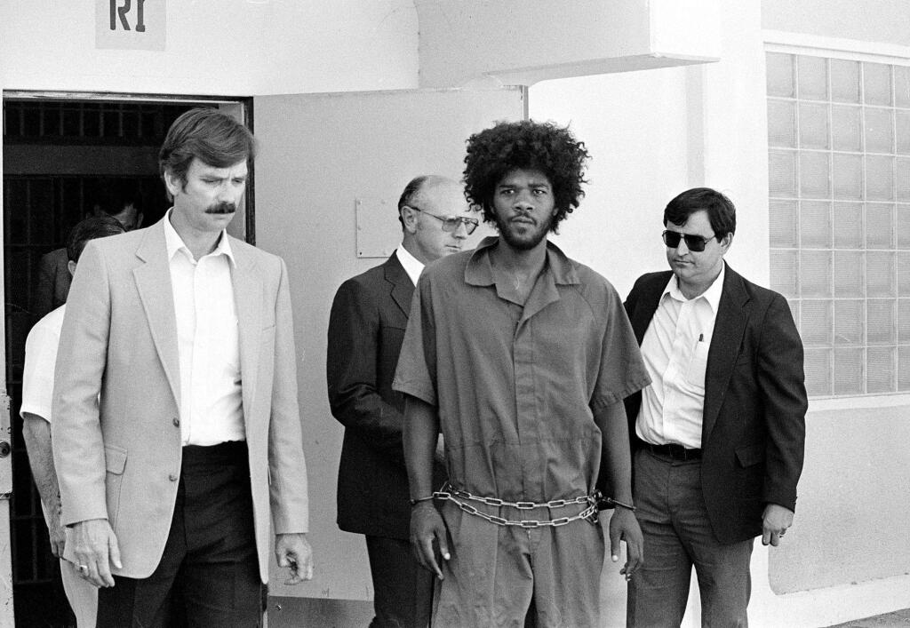 FILE - In this July 31, 1983, file photo, Kevin Cooper, center, a suspect in connection with the slashing death of four people in Chino, is escorted to a car for transport to San Bernadino from Santa Barbara, Calif., after he was arrested by police at Santa Cruz Island. U.S. Sen. Kamala Harris says California's governor should allow advanced DNA testing that advocates say could exonerate a death row inmate, Friday, May 18, 2018. The 60-year-old inmate was convicted of the 1983 Los Angeles-area hatchet and knife killings of four people. Kevin Cooper's clemency request is being reviewed by Gov. Jerry Brown's office. Two previous DNA tests concluded Cooper was the killer. California hasn't executed anyone since 2006. (AP Photo/File)