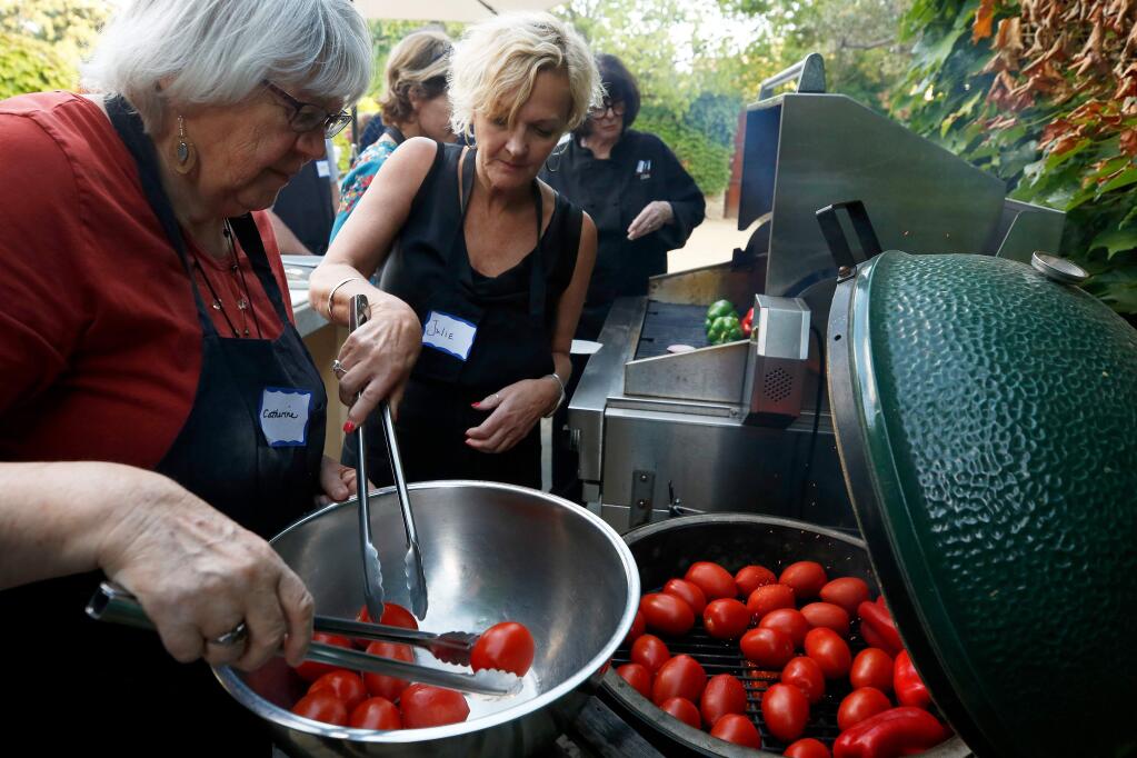Catherine Armstrong, left, of Sonoma, and Julie Vanderostyne, of Minneapolis, fill a barbecue grill with fresh tomatoes during a class about easy outdoor grilling with Chef Lisa Lavagetto at Ramekins in Sonoma on Thursday, June 13, 2019. (Alvin Jornada / The Press Democrat)