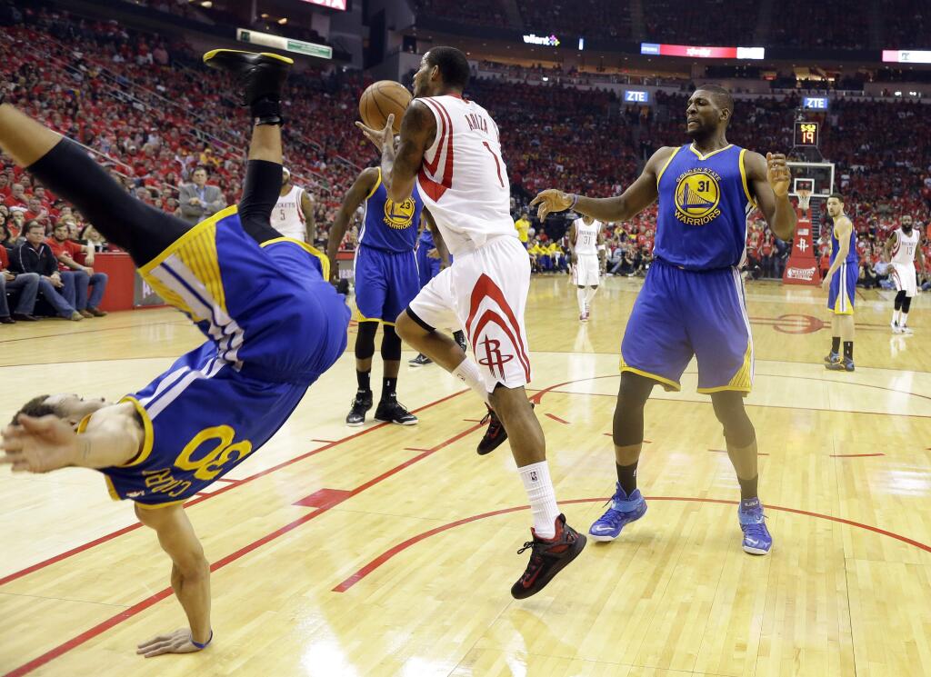 Golden State Warriors guard Stephen Curry (30) topples over Houston Rockets forward Trevor Ariza (1) during the first half in Game 4 of the Western Conference finals of the NBA basketball playoffs as center Festus Ezeli (31) looks on, Monday, May 25, 2015, in Houston. (AP Photo/David J. Phillip)