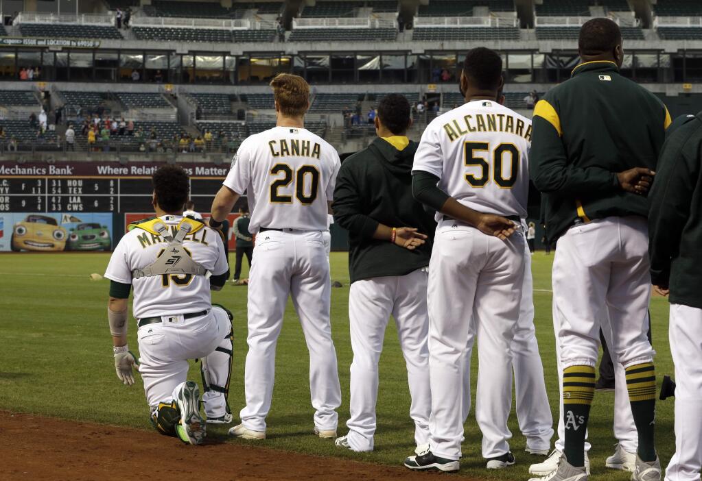 Oakland Athletics' Mark Canha (20) places his hand on the shoulder of Bruce Maxwell as Maxwell kneels during the national anthem for the third consecutive day, prior to the team's baseball game against the Seattle Mariners on Monday, Sept. 25, 2017, in Oakland, Calif. (AP Photo/Ben Margot)