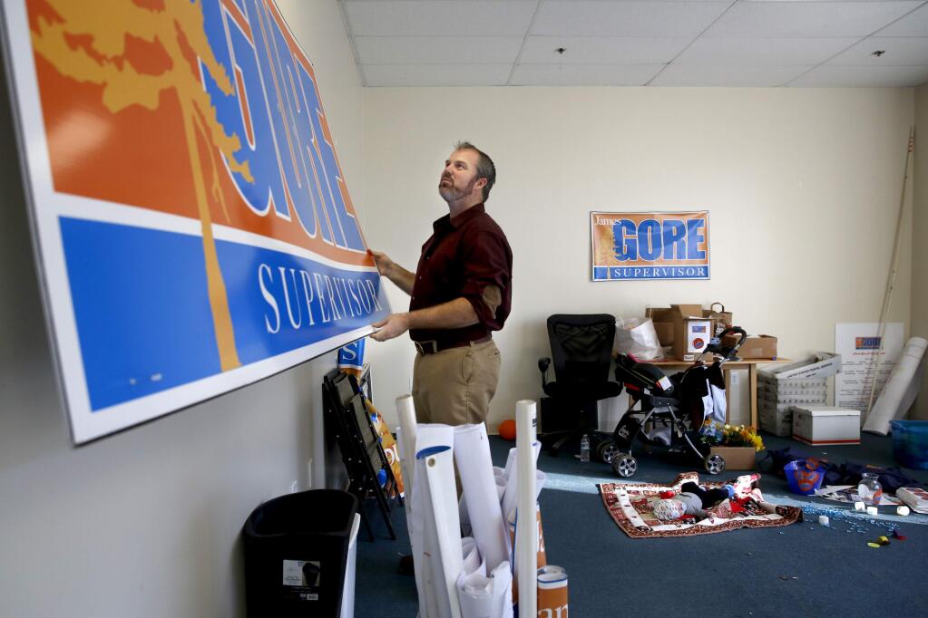 James Gore, the 4th District Supervisor-elect, takes down a campaign poster while his 10-week-old son, Jacob, right, rests on a blanket at his headquarters in Windsor, California on Sunday, November 30, 2014. (BETH SCHLANKER/ The Press Democrat)