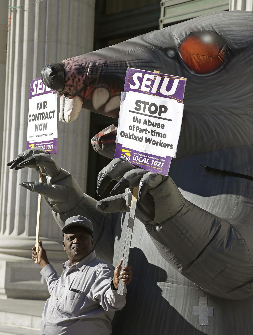 City of Oakland worker Melvin Beal places his picket signs in the paws of an inflatable rat in front of City Hall on Tuesday, Dec. 5, 2017, in Oakland, Calif. (AP Photo/Ben Margot)
