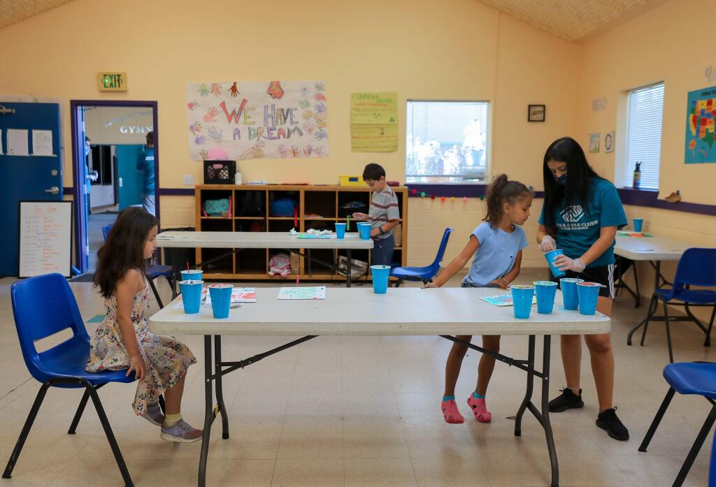 Brianna Farasat, right, helps Jealyn Fuller, 5, to make puffy paint, while separated Izilda Vicente, 6, sits at the other end of the table at the Boys & Girls Club, in Windsor on Monday, June 8, 2020. All staff members wear face masks, and campers are kept at the proper social distance.(Christopher Chung/ The Press Democrat)