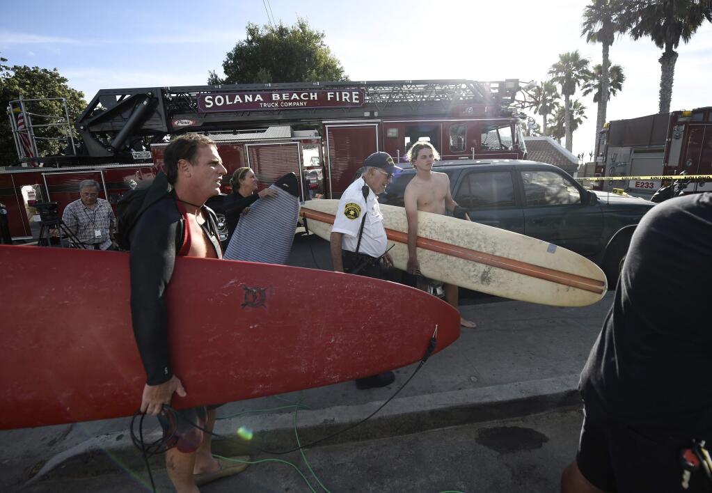 Surfers wait at the top of the stairs above the site of a cliff collapse at a popular beach Friday, Aug. 2, 2019, in Encinitas, Calif. At least one person was reportedly killed, and multiple people were injured, when an oceanfront bluff collapsed Friday at Grandview Beach in the Leucadia area of Encinitas, authorities said. (AP Photo/Denis Poroy)