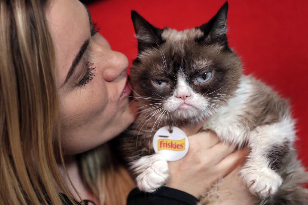 FILE - In this Nov. 14, 2016, file photo, Grumpy Cat poses for photos with her owner, Tabatha Bundesen, in New York. According to documents obtained by The Washington Post, Bundesen won a lawsuit first filed three years ago against the Grenade beverage company. She signed on for the cat to endorse a “Grumpy Cat Grumpuccino,” but the company subsequently used the cat's image to help sell other products, which an eight-person jury on Monday, Jan. 22, 2018, found was unauthorized. (AP Photo/Richard Drew, File)