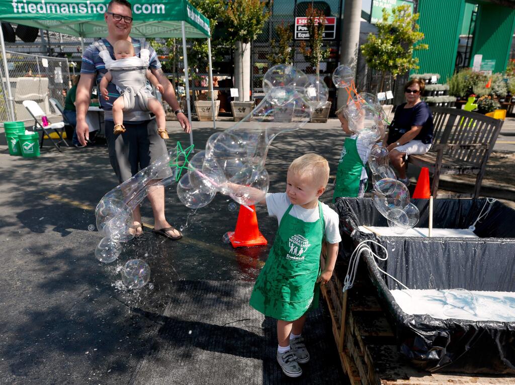 Judah Smith, 3, center, makes streams of bubbles with his brother Cyrus, 5, at right, while their father Ryan and little brother Reuben, 10 months, look on, during Friedman's Home Improvement Kidsworks 'Bubble It Up' event in Santa Rosa, California, on Saturday, July 6, 2019. (Alvin Jornada / The Press Democrat)