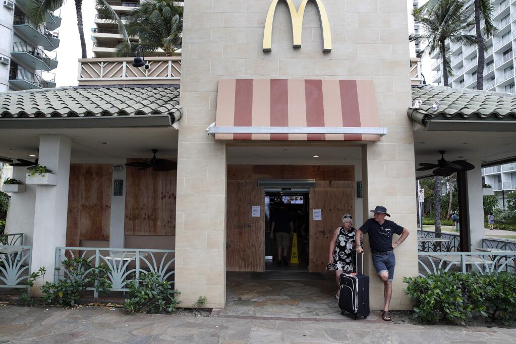 People stand outside of a partially boarded up McDonalds in preparation for Hurricane Lane, Thursday, Aug. 23, 2018, in Honolulu, Hawaii. The powerful hurricane unleashed torrents of rain and landslides Thursday that blocked roads on the rural Big Island but didn't scare tourists away from surfing and swimming at popular Honolulu beaches still preparing get pummeled by the erratic storm. (AP Photo/John Locher)