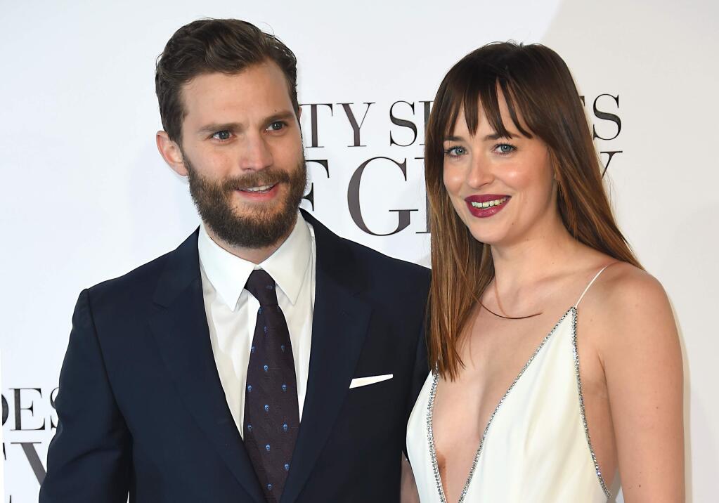 FILE - In this Feb. 12, 2015 file photo, actors Dakota Johnson, right, and Jamie Dornan pose for photographers at the UK Premiere of Fifty Shades of Grey, at a central London cinema. People might be a little more curious about “Fifty Shades Darker” than “Star Wars: The Force Awakens,” at least according to trailer views online. The ad for the steamy sequel to “Fifty Shades of Grey” netted a record-breaking 114 million views in its first 24 hours, surpassing “The Force Awakens'” 112 million views, according to Universal on Thursday, Sept. 15, 2015. (Photo by Jonathan Short/Invision/AP)