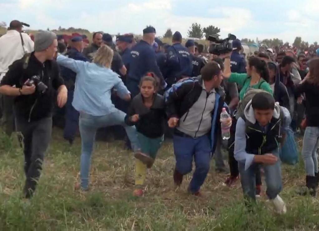 In this image taken from TV a Hungarian camerawoman, center left in blue, kicks out at a young migrant who had just crossed the border from Serbia near Roszke Hungary Tuesday Sept. 8, 2015. The camerawoman has been fired after she was caught on video kicking and tripping migrants entering Hungary across the border with Serbia. The N1TV Internet channel said their employee, widely identified in Hungarian media as Petra Laszlo, has been dismissed because she 'behaved unacceptably' at a makeshift gathering point where police take migrants immediately after they enter Hungary near the village of Roszke.(Index.Hu. via AP) HUNGARY OUT