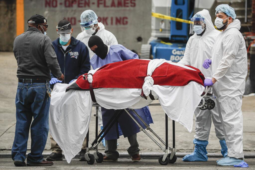 A body wrapped in plastic that was unloaded from a refrigerated truck is handled by medical workers wearing personal protective equipment due to COVID-19 concerns, Tuesday, March 31, 2020, at Brooklyn Hospital Center in Brooklyn borough of New York. The body was moved to a hearse to be removed to a mortuary. The new coronavirus causes mild or moderate symptoms for most people, but for some, especially older adults and people with existing health problems, it can cause more severe illness or death. (AP Photo/John Minchillo)