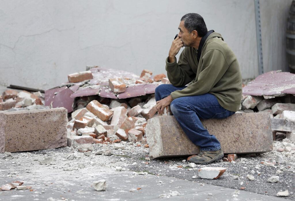 Ron Peralez, of Vacaville, Calif., sits on rubble and looks at earthquake-damaged buildings Monday, Aug. 25, 2014, in Napa, Calif. (AP Photo/Eric Risberg)