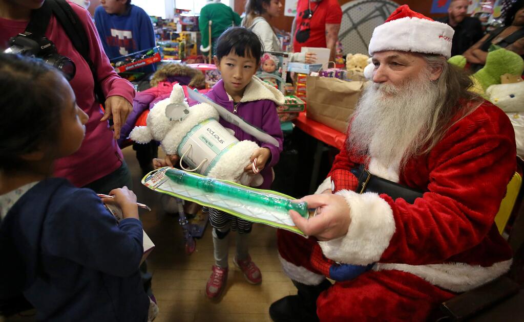 Richard 'Santa Claus' Stahl, right, hands out toys to sisters Yihyeon Son, 8, left, and Soeun Son, center, during the Guerneville Community Holiday Dinner held at the Guerneville Veterans Memorial Hall Thursday, December 25, 2014. (Crista Jeremiason / The Press Democrat)